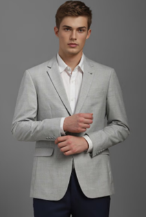Young man in a light gray blazer over a white shirt, poses confidently against a plain gray background. He has short brown hair and a serious expression.