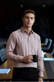 Young man in a light pink shirt holding a black coffee mug, standing in a modern office with a long wooden table.