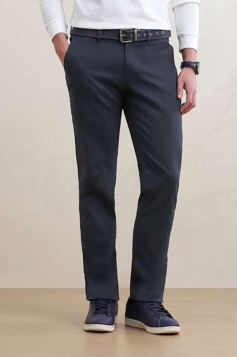 Man wearing dark navy slim-fit trousers with a black belt, white shirt, watch, and navy sneakers.