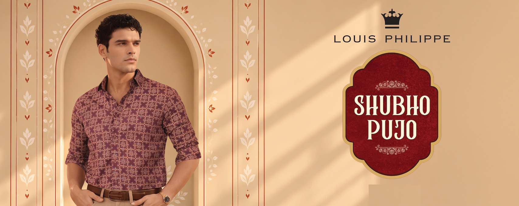 A man in a patterned traditional outfit stands in an ornate arch beside a red “Shubh Pujo” greeting, with warm sunlight creating a festive Bengali Puja mood.